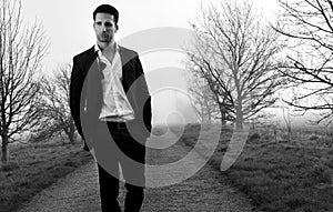 Handsome man wearing suit walking on a lonely foggy road