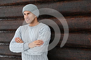 Handsome man wearing warm sweater and hat near wall, space for text. Winter season