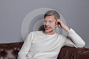 Handsome man wearing white sweater sitting on the leather sofa. Comfort and relaxation