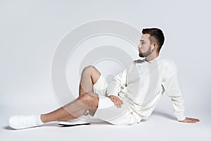 Handsome man wearing white sweatshirt and shorts with wireless earbuds sitting