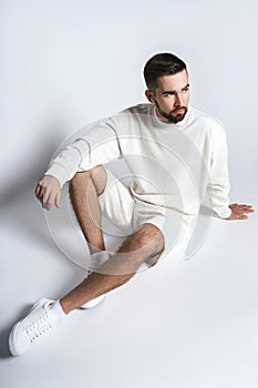 Handsome man wearing white sweatshirt and shorts with wireless earbuds sitting