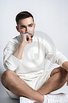 Handsome man wearing white sweatshirt and shorts with wireless earbuds sitting