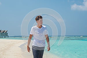 Handsome man wearing white t-shirt and black shorts walking on the tropical beach at the island luxury resort