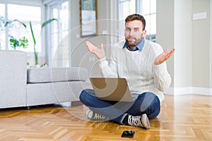 Handsome man wearing working using computer laptop clueless and confused expression with arms and hands raised