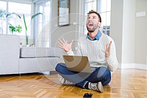 Handsome man wearing working using computer laptop crazy and mad shouting and yelling with aggressive expression and arms raised