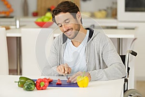 Handsome man in wheelchair cuts pepers with knife