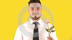 Handsome Man in a White Shirt and Tie Sniffing a Rose on a Yellow Background.