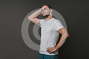 A handsome man in a white t-shirt and jeans stands on a gray background. Studio photo