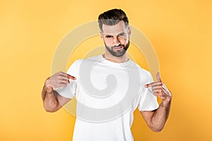 Handsome man in white t-shirt pointing with fingers at himself isolated on yellow photo