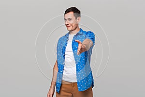 Handsome man in a white tee and blue shirt offers hand for shake isolated over grey background.
