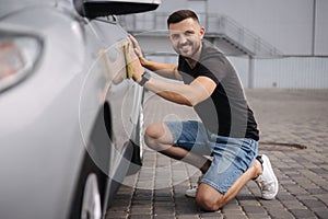 Handsome man wipes a car with a rag in a showroom at a self-service car wash. Gray car