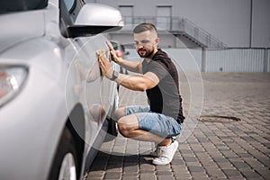 Handsome man wipes a car with a rag in a showroom at a self-service car wash. Gray car