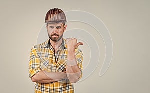 handsome man worker in construction safety helmet and checkered shirt on building site pointing finegr, copy space, ad