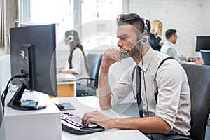 Handsome man working in call center. Customer support operator with headset working in office with his colleagues.