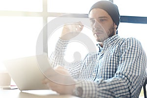 Handsome man working from his home office. Analyze business plans on laptop. Blurred background, film effect