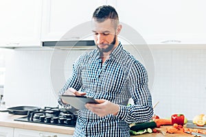 Handsome man working in kitchen, looking up on the internet receipes. Details of modern cook working with tablet