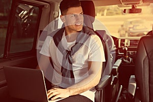 Handsome man working with laptop on backseat of car