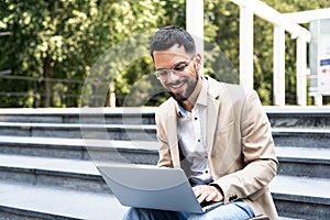 Handsome man working on laptop in city street. Man using his knowledge while sitting on stairs outdoors. Businessman successful