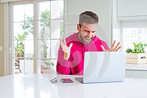 Handsome man working using computer laptop celebrating mad and crazy for success with arms raised and closed eyes screaming