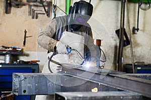 Handsome man workshop welding iron spark fire hot steel with a power GMAW welder and protective gear