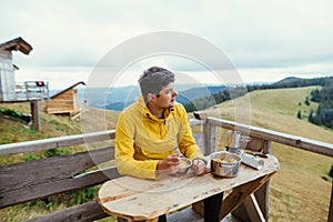 Handsome man in a yellow jacket eats in the mountains on the terrace of a country house and looks away with a smile on his face