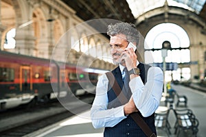 Mature businessman with smartphone on a train station.