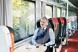 Mature businessman with smartphone travelling by train.