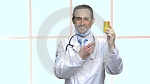 Handsome mature doctor showing bottle of pills.