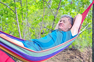 Handsome mature elderly man resting in a hammock in a forest