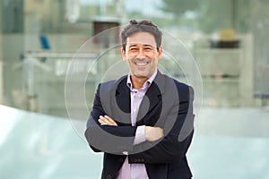 Handsome mature man in business suit posing with arms crossed outdoors and smiling