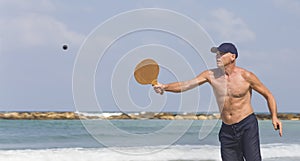 A handsome mature man hits a ball while playing matkot on the beach