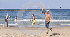 A handsome mature man hits a ball while playing matkot on the beach