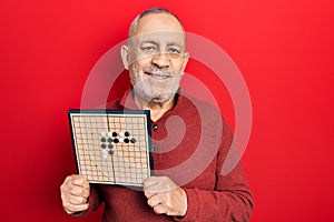 Handsome mature man holding asian go game board smiling with a happy and cool smile on face