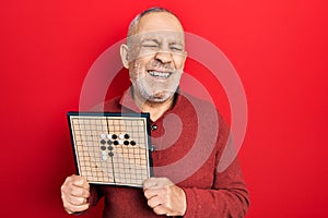 Handsome mature man holding asian go game board smiling and laughing hard out loud because funny crazy joke