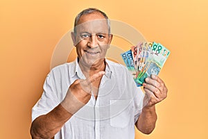 Handsome mature man holding australian dollars smiling happy pointing with hand and finger