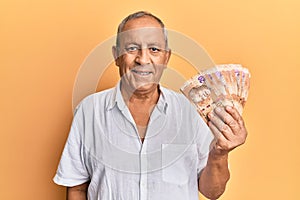 Handsome mature man holding south african 20 rand banknotes looking positive and happy standing and smiling with a confident smile