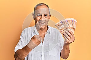 Handsome mature man holding south african 20 rand banknotes smiling happy pointing with hand and finger