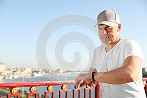 Handsome mature man looking at fitness tracker on bridge. Healthy lifestyle