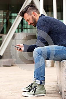 Handsome mature man sitting by the street using cellphone