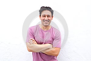 Handsome mature man standing and smiling with arms crossed against white wall