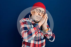 Handsome mature man wearing hipster look with wool cap sleeping tired dreaming and posing with hands together while smiling with