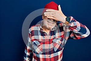 Handsome mature man wearing hipster look with wool cap smiling and laughing with hand on face covering eyes for surprise