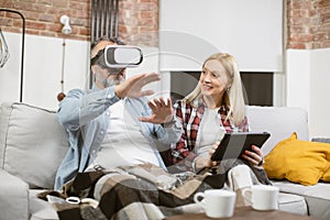 Man sitting on couch in VR headset while woman using tablet