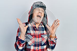 Handsome mature man wearing winter hat with ear flaps celebrating mad and crazy for success with arms raised and closed eyes