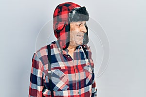 Handsome mature man wearing winter hat with ear flaps looking away to side with smile on face, natural expression