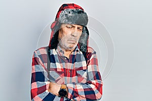Handsome mature man wearing winter hat with ear flaps skeptic and nervous, disapproving expression on face with crossed arms