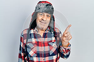 Handsome mature man wearing winter hat with ear flaps smiling happy pointing with hand and finger to the side