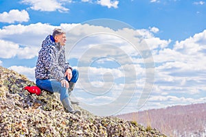 A handsome mature tourist sitting on a rock looks