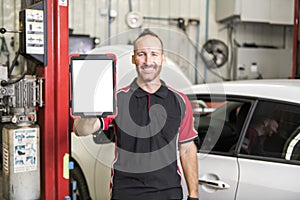 Handsome mechanic based on car in auto repair shop with tablet on hand