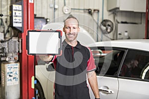 Handsome mechanic based on car in auto repair shop with tablet on hand